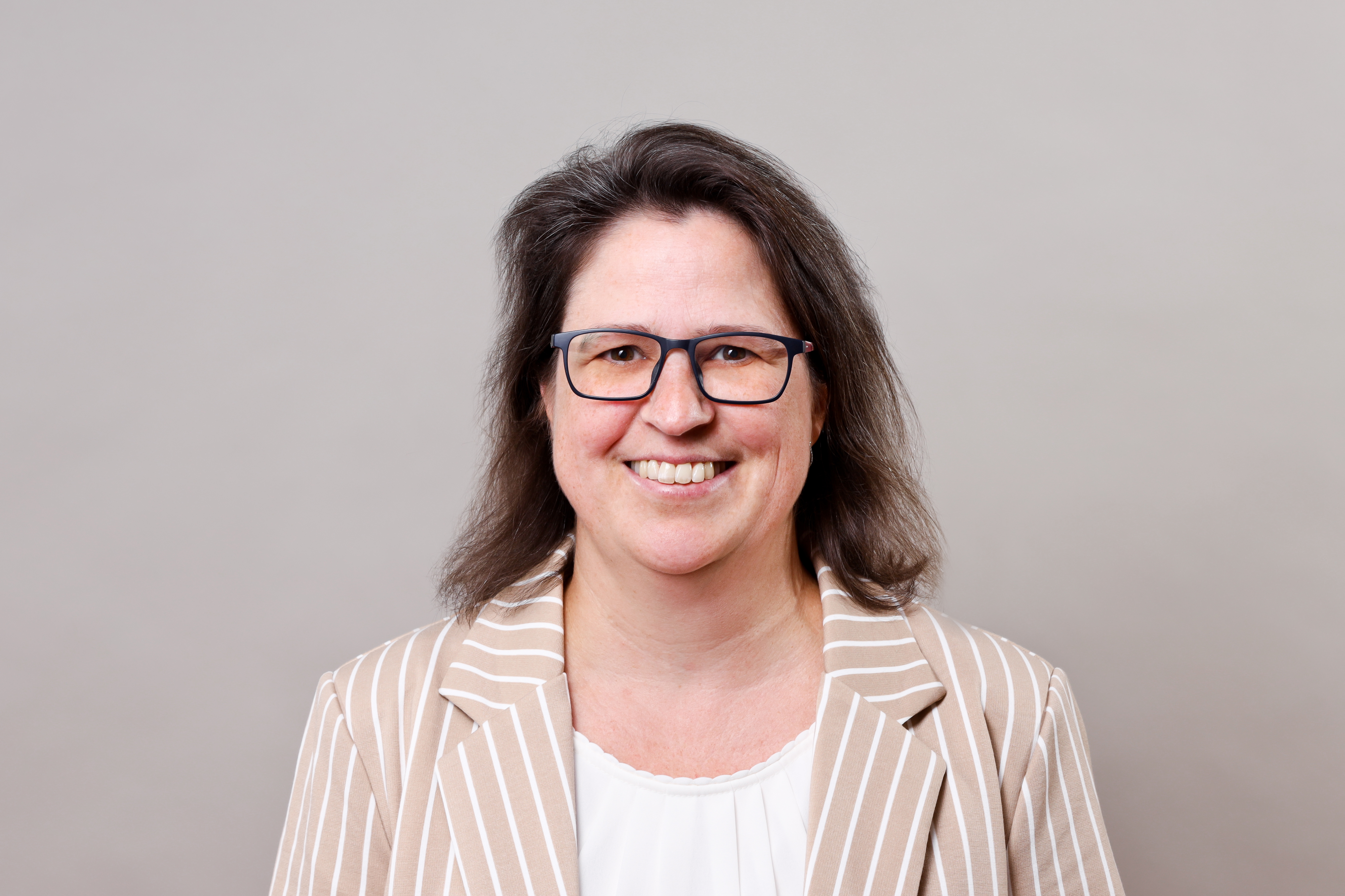 Frau mit Brille und dunklen Haaren, heller Blazer und weißer Bluse