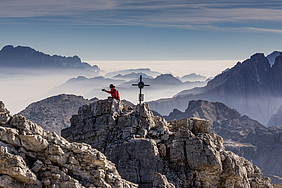 Mensch auf Bergspitze mit Gipfelkreuz