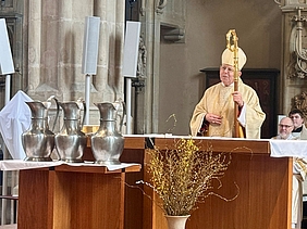 Bischof am Altar, vor dem drei große Ölkannen stehen