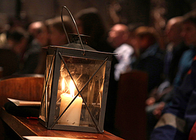 Brennende Kerze in einer Laterne auf einer Kirchenbank