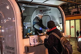 Detailaufnahme eines Wärmemobils; ein Mann reicht einem anderen etwas über die Theke