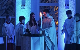 ein Priester und Jugendliche mit einer Osterkerze