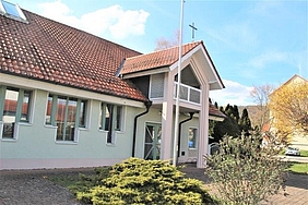 Haus mit rotem Dach, grünen Fenstern und Kreuz auf Dach
