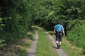 Mann mit Wanderrucksack und Hut auf Wanderweg